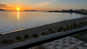 A beach with a sunset, calm water, and distant buildings.