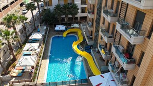 A rooftop pool with a yellow slide, surrounded by lounge chairs and umbrellas.