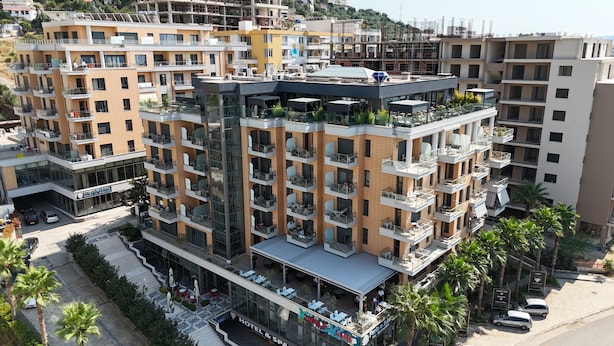 A multi-story hotel with balconies, a rooftop terrace, and a ground-level restaurant/lounge area.