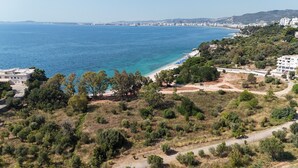 A coastal landscape with a beach, dense greenery, and a cityscape in the background.