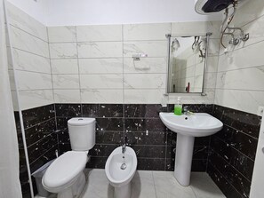 Une salle de bain équipée de toilettes, d’un bidet et d’un lavabo, et dont le sol et les murs sont recouverts de marbre et de carreaux noirs.