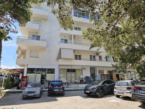 Un immeuble à plusieurs étages, doté d’une entrée au niveau du sol, de plusieurs balcons et d’un espace de stationnement où sont garées des voitures.