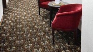 A hotel hallway with patterned carpet, red chairs, and framed artwork on the walls. - Great Polonia Kraków Kazimierz  (Kraków)