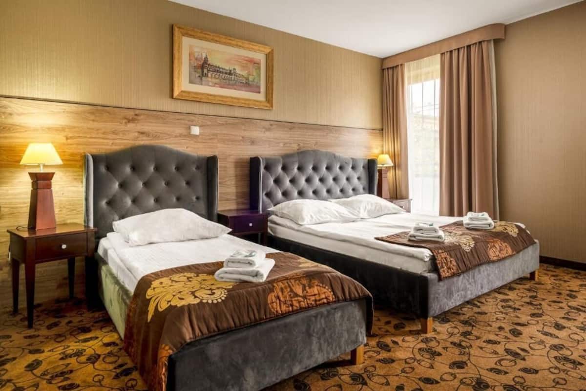 A hotel room with two beds, wooden headboards, a framed picture on the wall, and a patterned carpet.