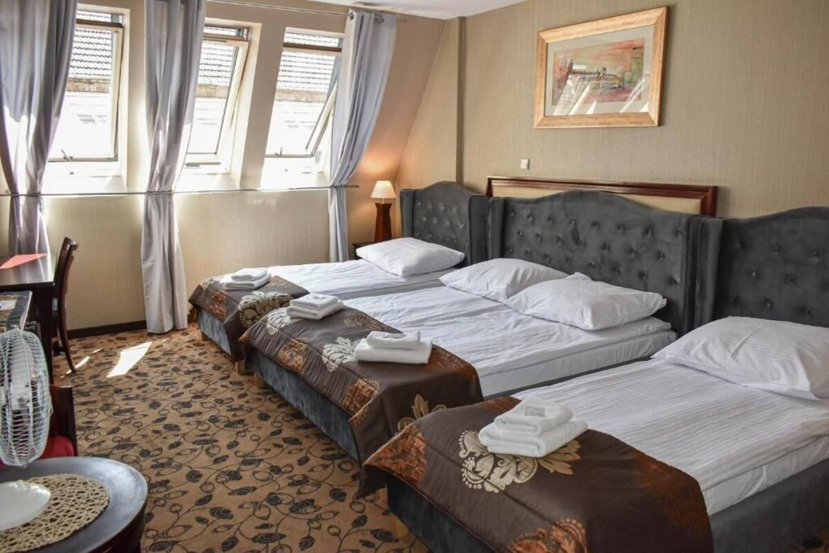 A hotel room with three beds, a dining table, and a chair.