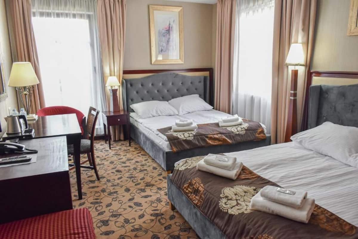 A hotel room with two beds, a desk, a chair, and a lamp.