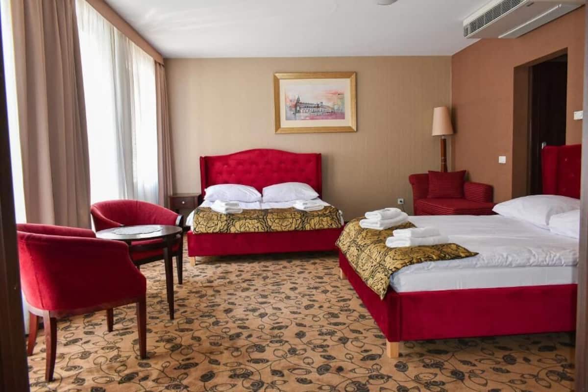 A hotel room with two beds, a red chair, a small table, and a patterned carpet.