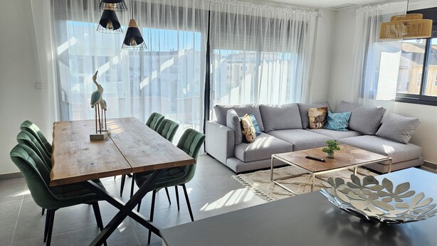 A modern living room with a dining area, featuring a wooden table, green upholstered chairs, a grey sofa with decorative pillows, and a coffee table. - Modern penthouse close to Arenal beach with big top veranda. (Jávea)
