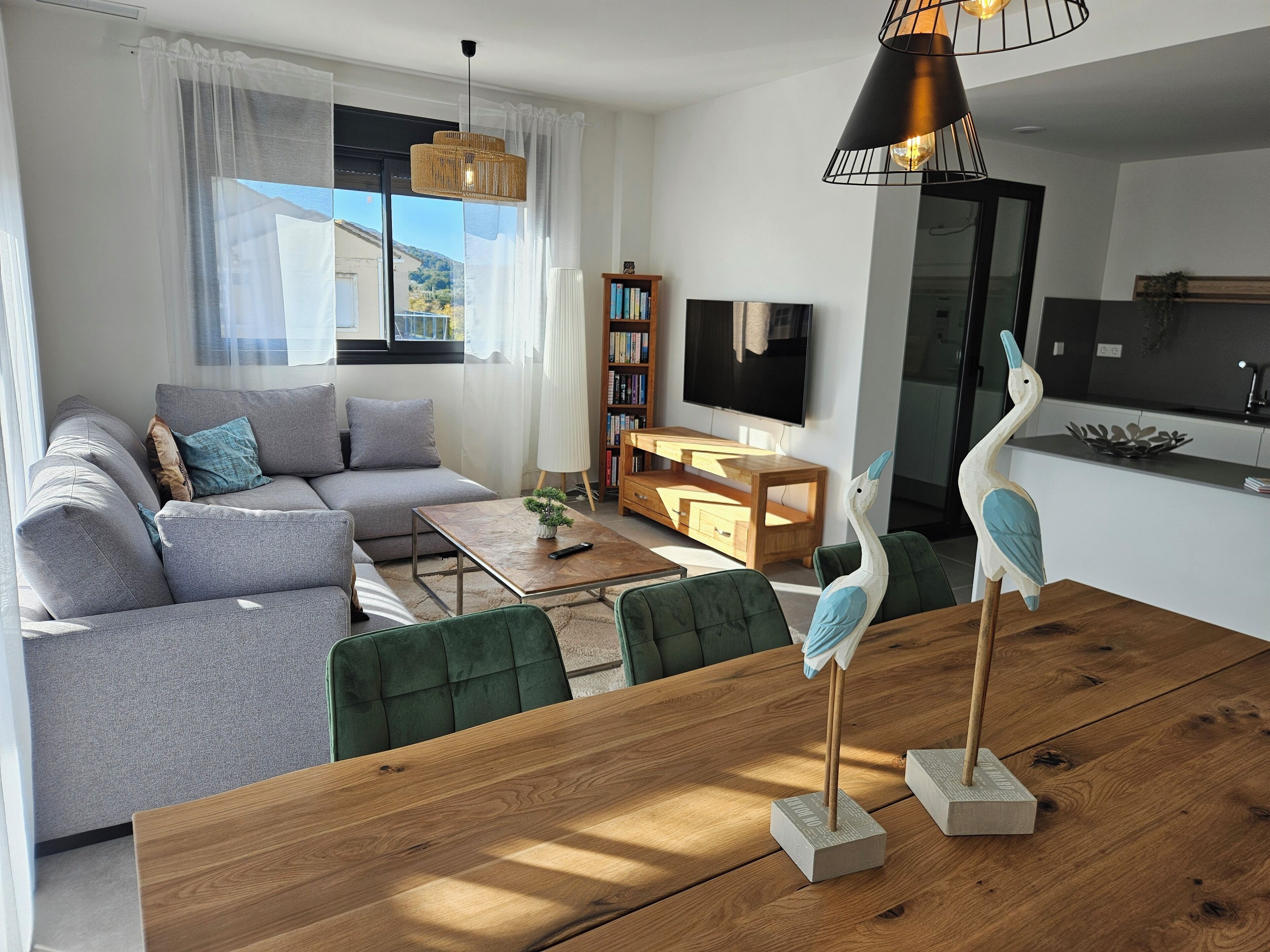 A modern living room with a grey sofa, wooden coffee table, and a dining table with two bird sculptures.