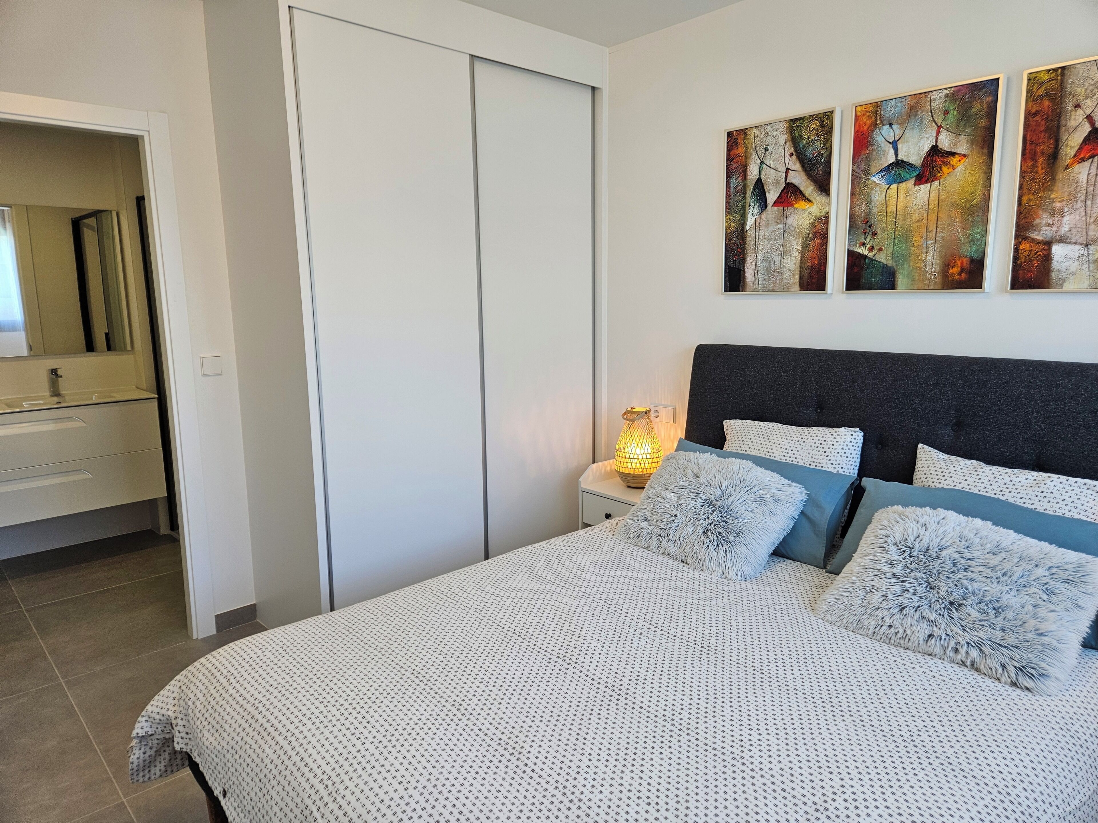 Un dormitorio con cama, mesitas de noche, un espejo y obras de arte en la pared.