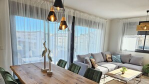 A modern living room with a wooden dining table, green upholstered chairs, a grey sofa with decorative pillows, and a coffee table. - Modern penthouse close to Arenal beach with big top veranda. (Jávea)