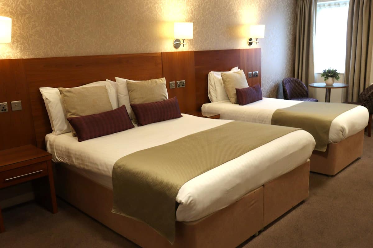 Une chambre d’hôtel avec deux lits, une table de chevet, une lampe et une fenêtre avec des rideaux.