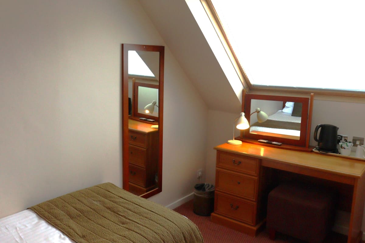 Une pièce comprenant un lit, un bureau, une chaise, un miroir, une lampe et une fenêtre.