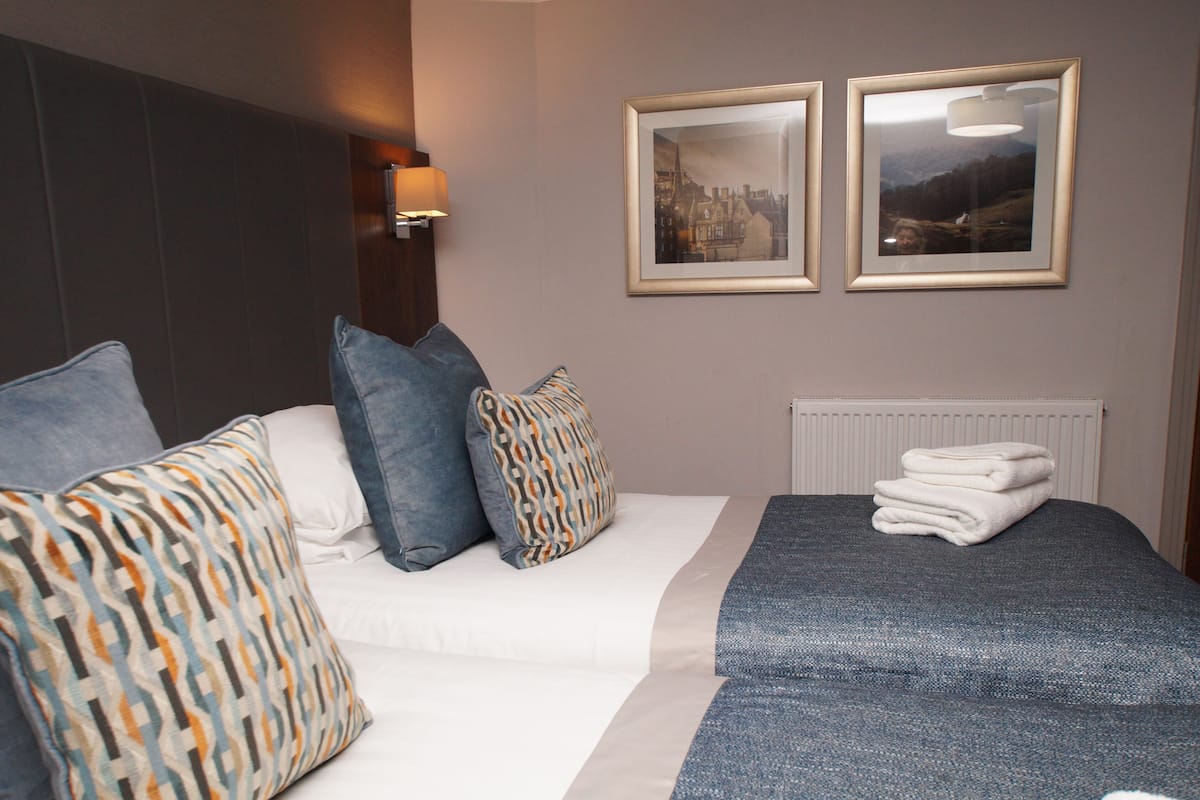 Une chambre d’hôtel avec un lit, des oreillers, une couverture, un radiateur et deux tableaux encadrés au mur.
