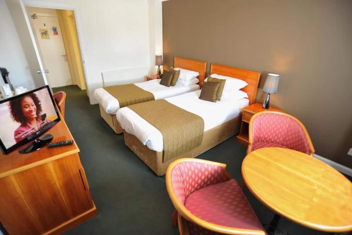 Une chambre d’hôtel avec deux lits, un bureau avec une télévision, une chaise et une petite table.