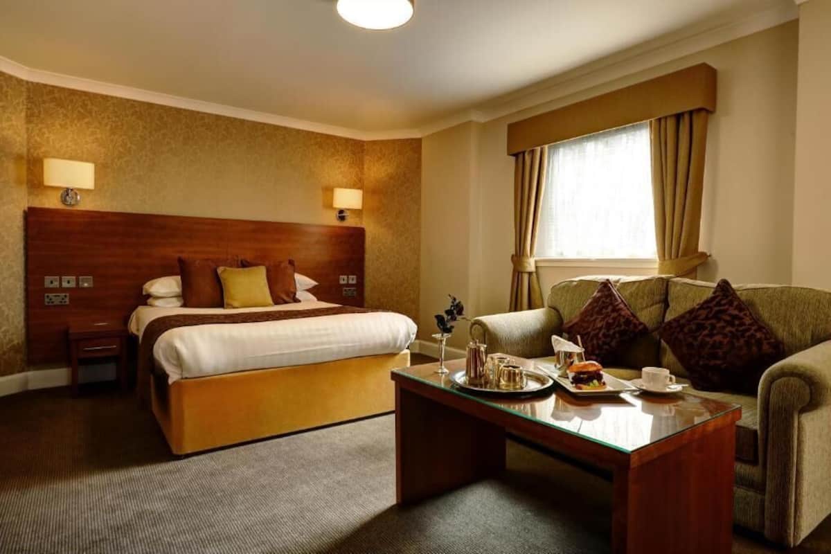 Une chambre d’hôtel avec un grand lit, un canapé, une table basse avec des éléments pour le petit-déjeuner et une fenêtre avec des rideaux.