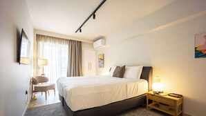 A hotel room with a bed, bedside table, lamp, chair, and a painting on the wall.