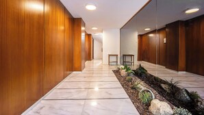 A modern hallway with wooden paneling and a marble floor, leading to a door at the end.