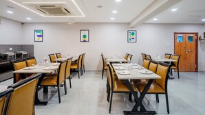 A dining area with multiple tables and chairs, a ceiling fan, recessed lighting, and framed artwork on the walls. - Treebo Pride inn Raidurg (Hyderabad)
