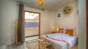 A bedroom with a bed, a small table, a decorative wall piece, and a view of the outside. - Riad Amirkesh and Pool (Marrakech)