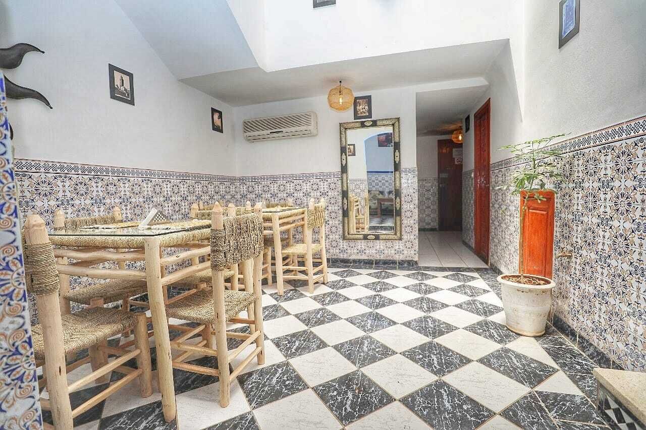 A dining area with a checkered floor, rattan chairs, and a tiled wall with a decorative border.