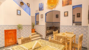 A traditional interior with a checkered floor, a wooden table with woven chairs, a staircase with blue railings, and tiled walls. - Riad Amirkesh and Pool (Marrakech)