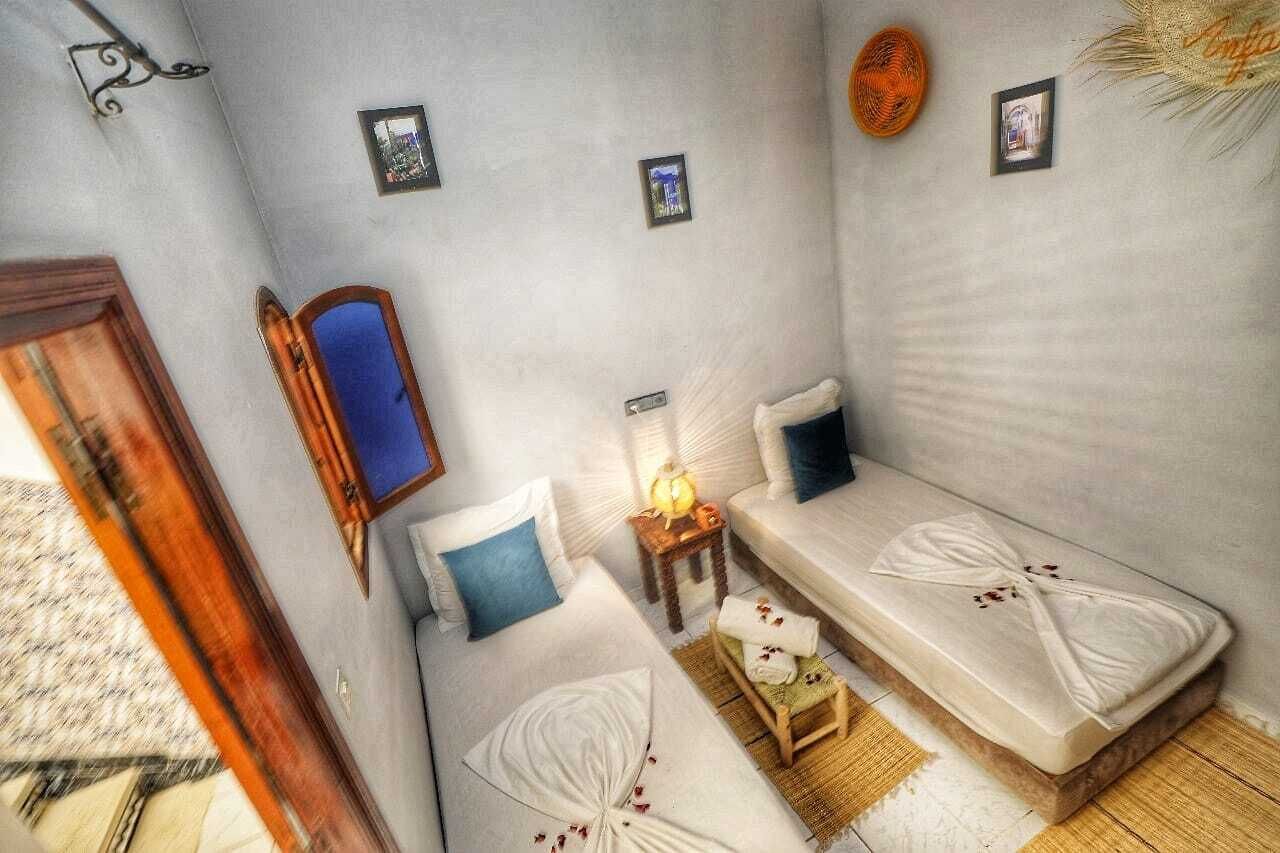 Une petite pièce accueillante avec deux lits, une porte en bois, un miroir et une petite table avec une lampe.