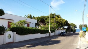 A quiet residential street with a white house, a car parked on the side, and a blue directional sign. - Appartamenti Costa Sud Gallipoli (Torre Suda)
