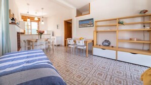 A room with a bed, a dining table with chairs, a kitchen area, and a shelf with decorative items. - Appartamenti Costa Sud Gallipoli (Torre Suda)