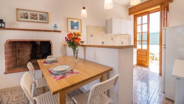 A dining area with a wooden table, white chairs, a vase with flowers, and hanging pendant lights. - Appartamenti Costa Sud Gallipoli (Torre Suda)
