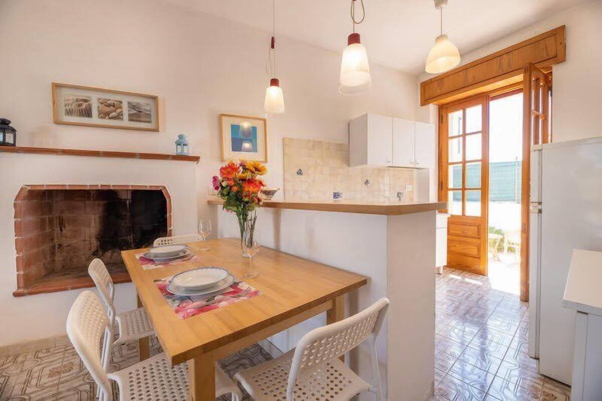 A dining area with a wooden table, white chairs, a vase with flowers, and hanging pendant lights.