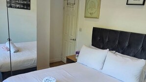 A neatly made bed with white linens and two towels, a dark headboard, a framed picture on the wall, and a door with a mirror reflecting a cityscape. - London Charm - Moscow Road Apartment (London)