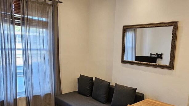A modern living room with a grey sofa, wooden dining table, and a mirror on the wall. - London Charm - Moscow Road Apartment (London)
