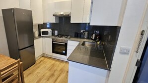A compact kitchen with a refrigerator, microwave, oven, and a small dining area with a table and chairs. - London Charm - Moscow Road Apartment (London)