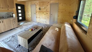 Un intérieur en bois comprenant un canapé, une table basse, un coin cuisine et une vue par une fenêtre.