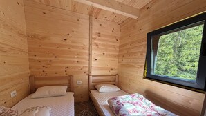 Une cabane avec deux lits superposés en bois, une fenêtre donnant sur la forêt et un petit tapis sur le sol.