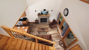 A spacious living area with a fireplace, wooden flooring, a staircase, and a view of the outdoors. - Smokey's Hideaway: Your Secret in the Smokies (Sevierville)