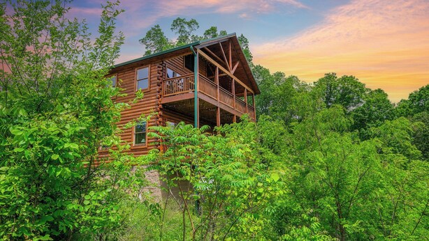 A log cabin with a balcony, surrounded by dense greenery. - Smokey's Hideaway: Your Secret in the Smokies (Sevierville)