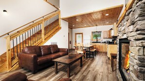 A spacious living area with a wooden staircase, a stone fireplace, and a kitchen with wooden cabinets. - Smokey's Hideaway: Your Secret in the Smokies (Sevierville)
