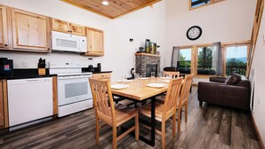 A modern kitchen with wooden cabinets, a microwave, and a stove. There is a dining area with a table and chairs, and a living area with a couch and a fireplace. - Smokey's Hideaway: Your Secret in the Smokies (Sevierville)