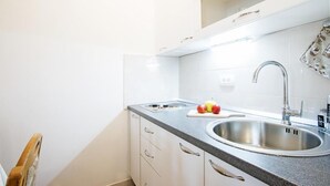 Eine moderne Küche mit Spüle aus Edelstahl, einer Arbeitsplatte mit Schneidebrett und Äpfeln sowie weißen Schränken.