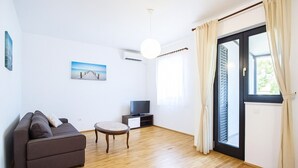 Ein modernes Wohnzimmer mit einer Couch, einem kleinen Tisch, einem Fernseher und einem großen Fenster mit Vorhängen.