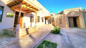 A building with a covered entrance, steps leading to a door, and a small garden area. - Ancient Tagayev Hotel (Bukhara)