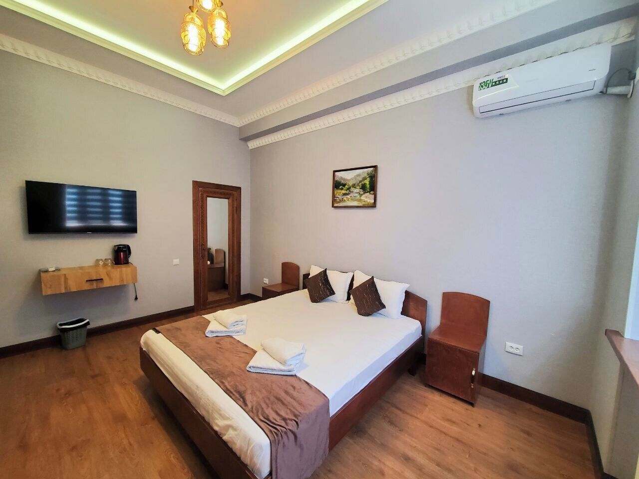 A hotel room with a large bed, a flat-screen TV, a wooden cabinet, and an air conditioning unit.