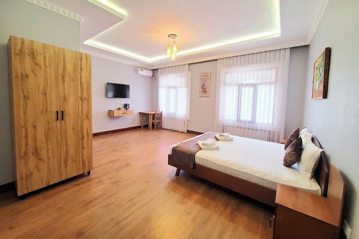 Amplia habitación de hotel con una cama grande, armario de madera, un escritorio y un televisor montado en la pared.
