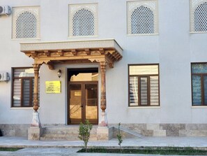 A building with a covered entrance, a sign indicating it is a family guest house, and a small garden area in front. - Ancient Tagayev Hotel (Bukhara)