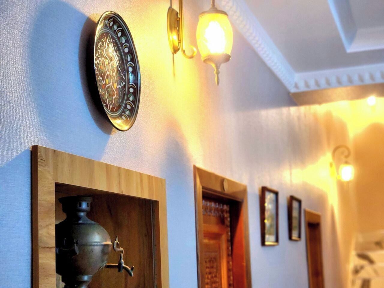 A hallway with a decorative metal plate, a wall-mounted light fixture, and a wooden cabinet with a metal object inside.
