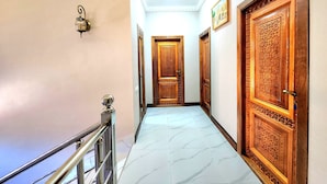 A hallway with ornate wooden doors, a marble floor, and a metal railing. - Ancient Tagayev Hotel (Bukhara)