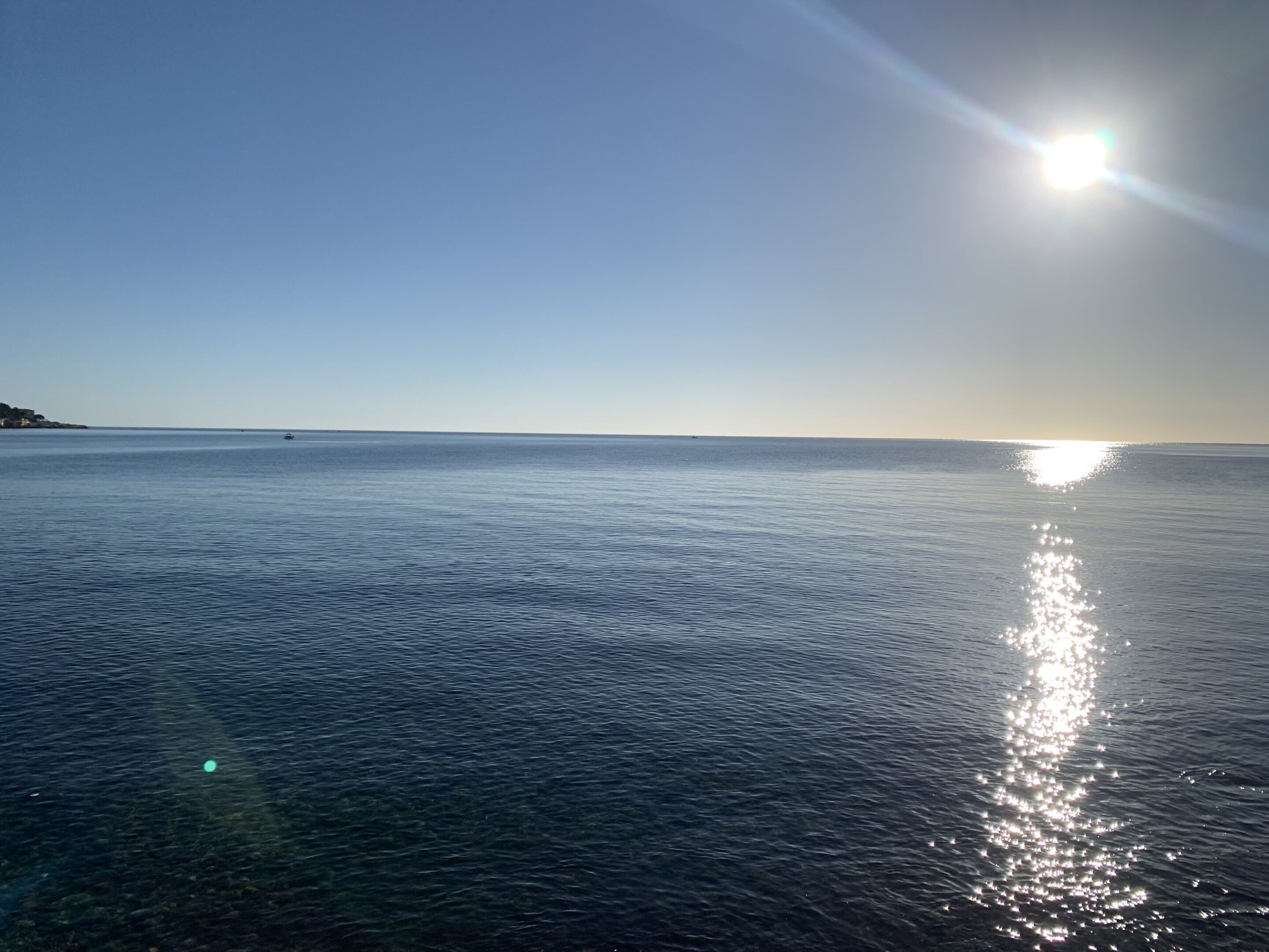 Mar calmo com céu claro e sol brilhante refletindo na água.