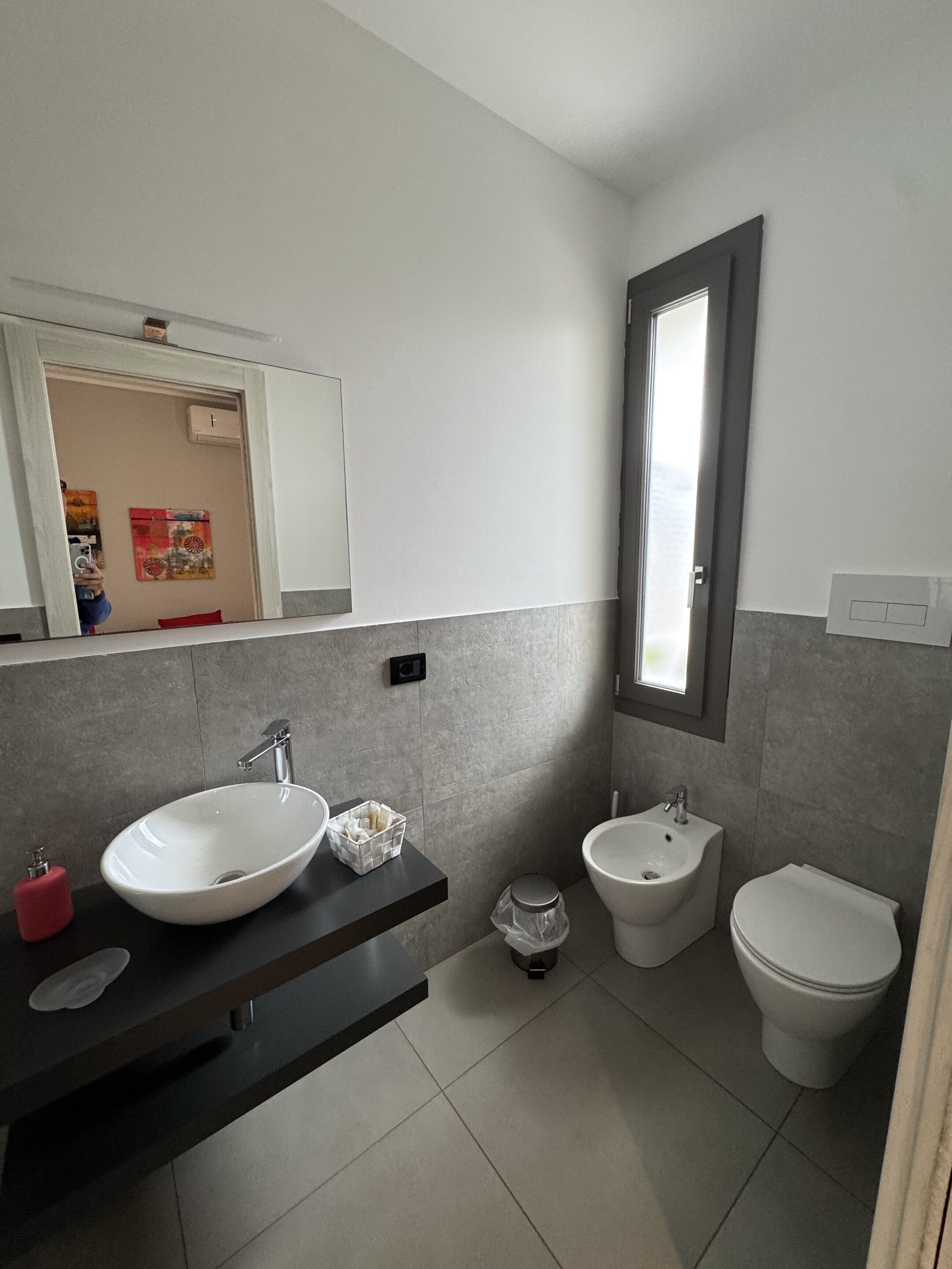 A modern bathroom with a large mirror, a vessel sink, a bidet, and a toilet.